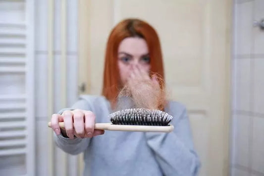 Eine Frau betrachtet eine Haarbürste voller Haare, da sie Haarausfall hat